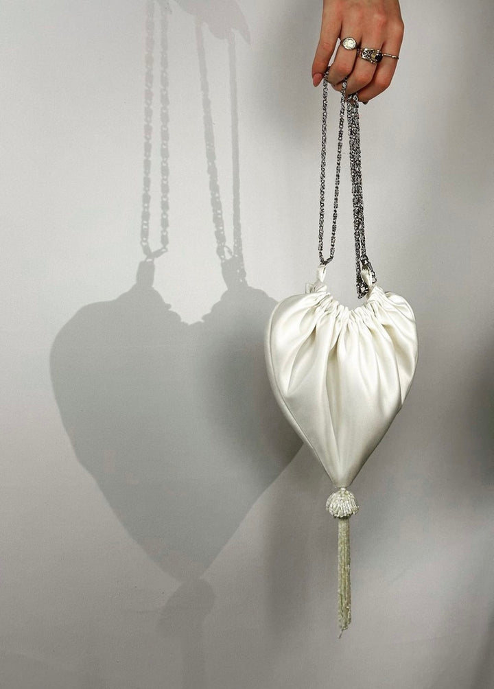 This super chic white satin bag, shaped like a heart, boasts a silver chain handle and a stylish tassel for the perfect finishing touch